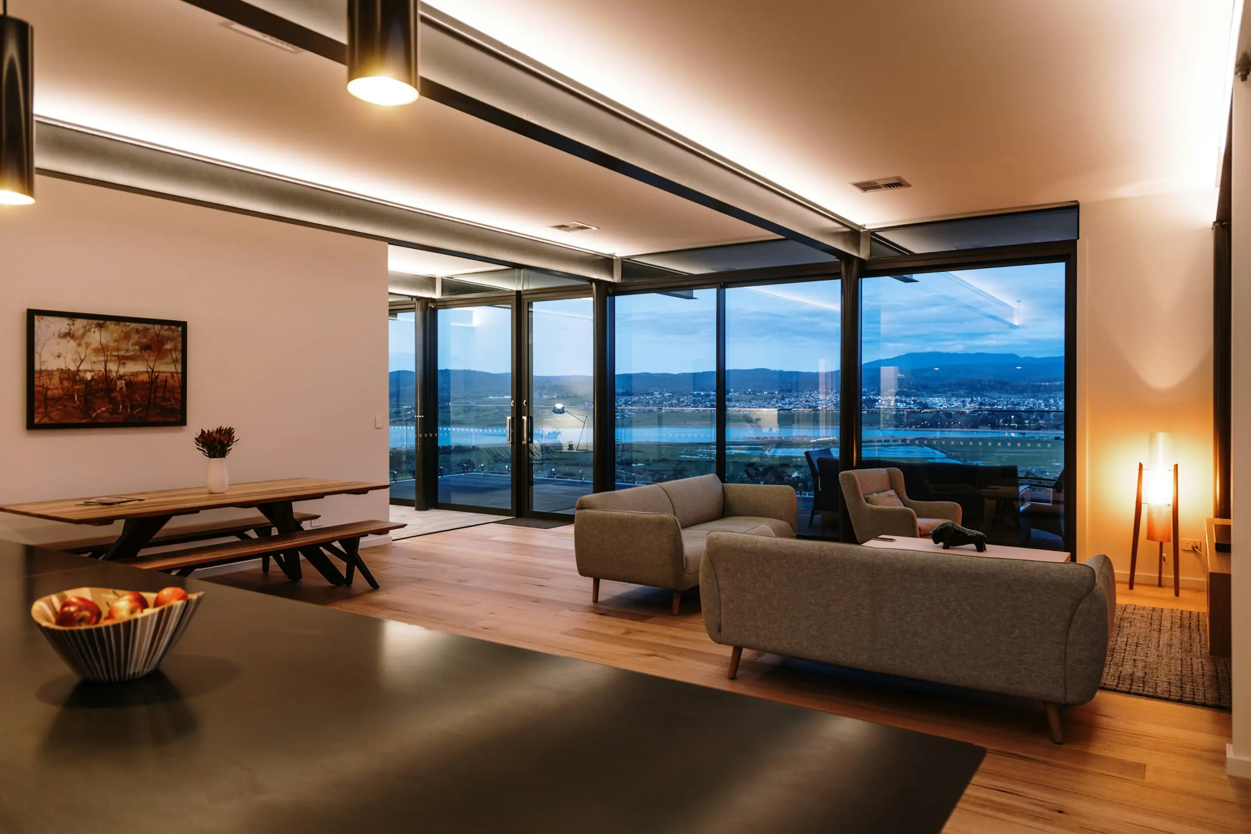 Warmly lit open-plan living room at dusk with floor-to-ceiling glazing