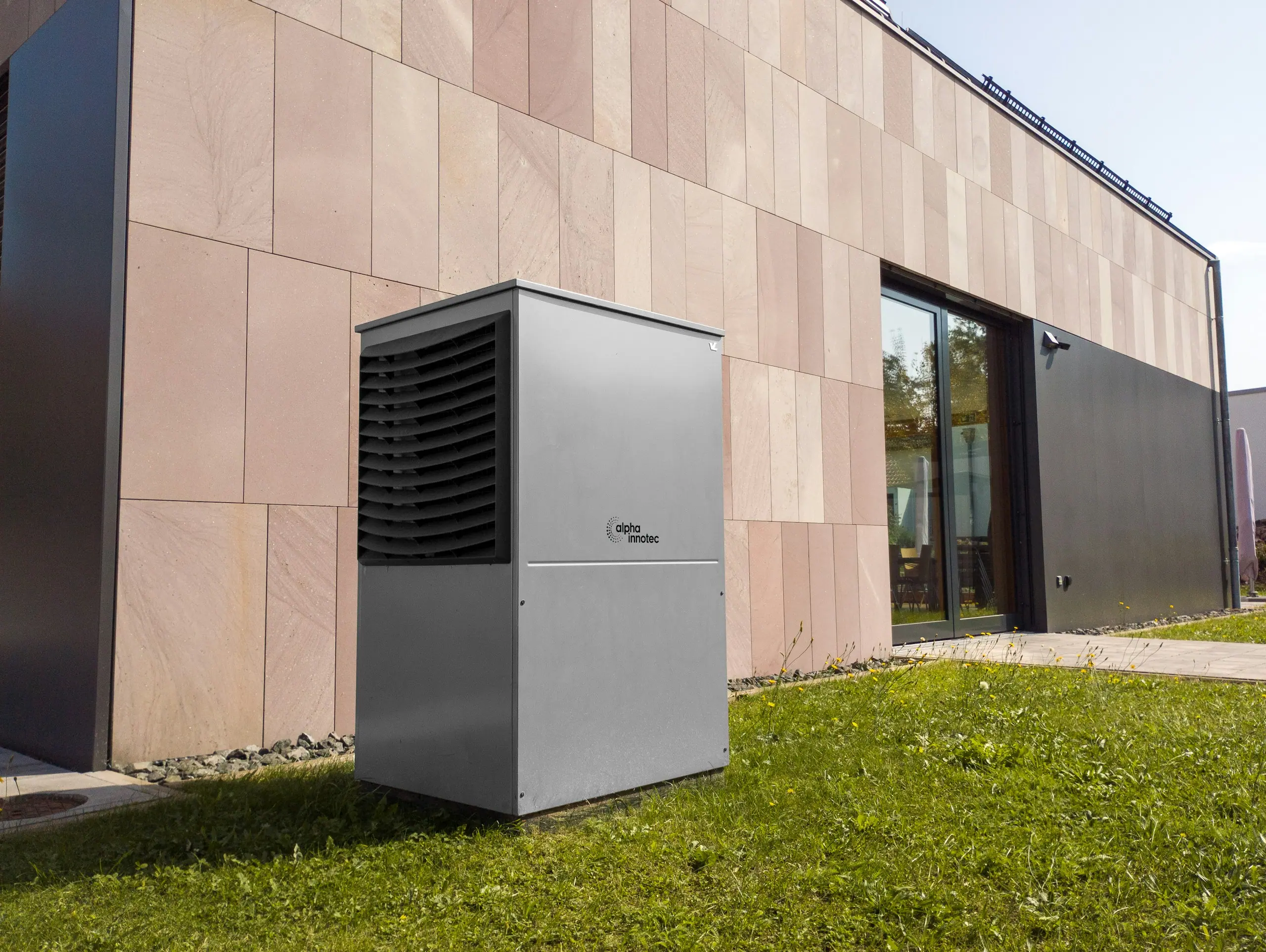 Modern air source heat pump unit beside a stone-clad house